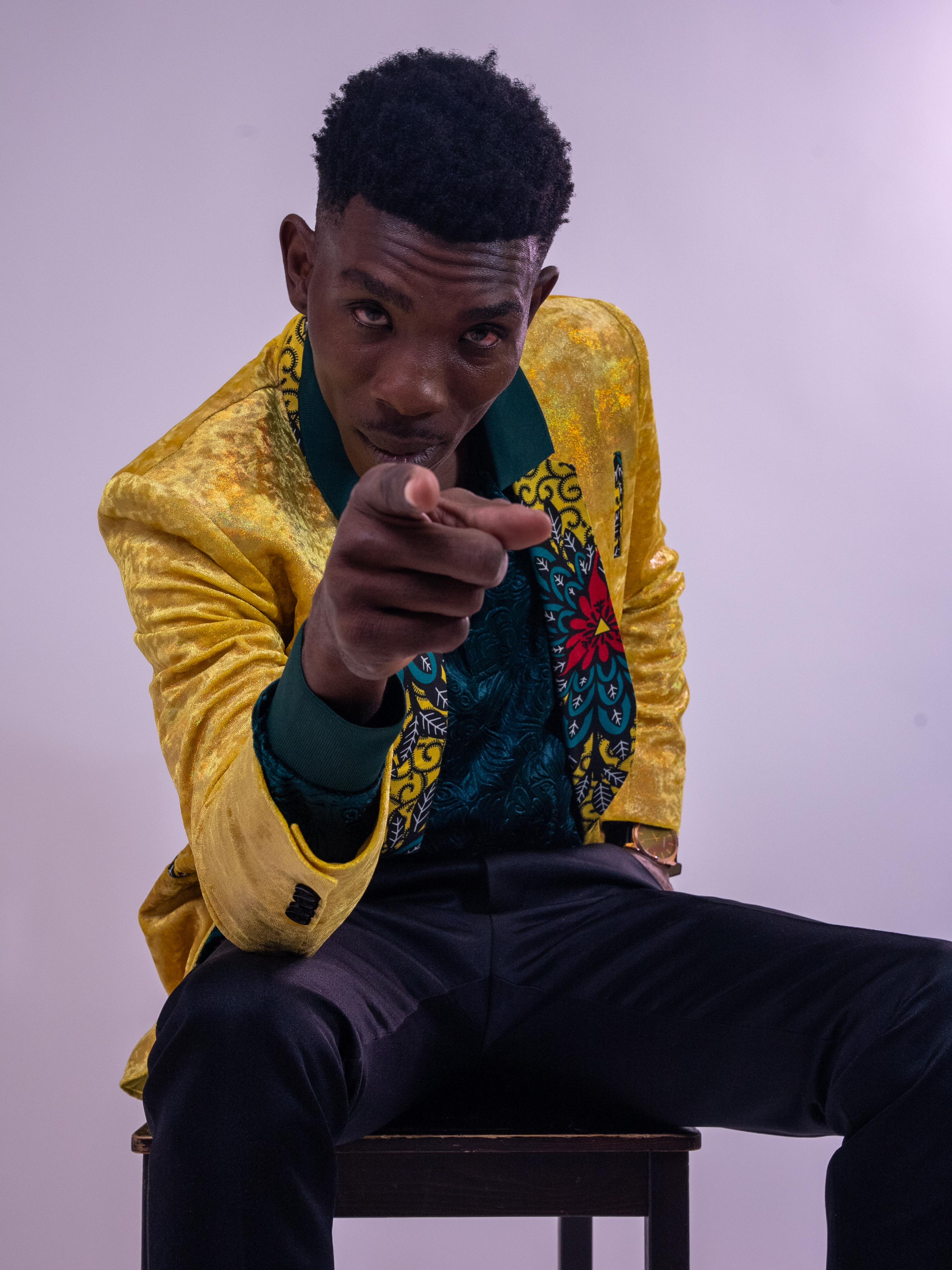 Seated portrait in a yellow jacket, pointing toward the camera